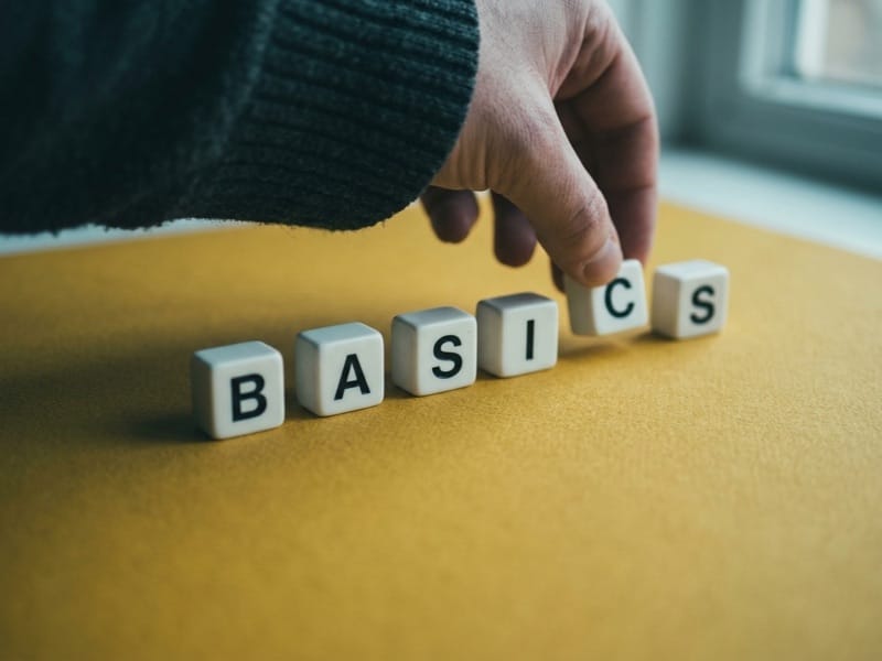 Hand arranging wooden letter cubes spelling the word basics on a yellow surface