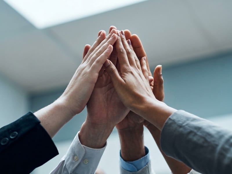 Several coworkers joining hands in a high five above an office table