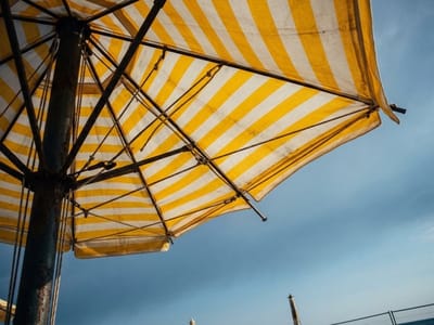 Yellow and white striped beach umbrella seen from below against a cloudy sky