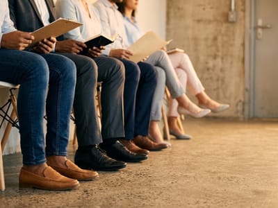 Row of seated people holding folders and tablets while waiting in chairs