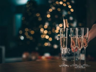 Champagne flutes on a table in front of a blurred, lit Christmas tree